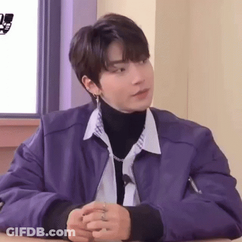 A Young Man Wearing A Purple Jacket And A Turtleneck Is Sitting At A Table . GIF