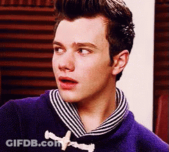 A Young Man Wearing A Purple Sweater And A Striped Scarf Looks At The Camera . GIF