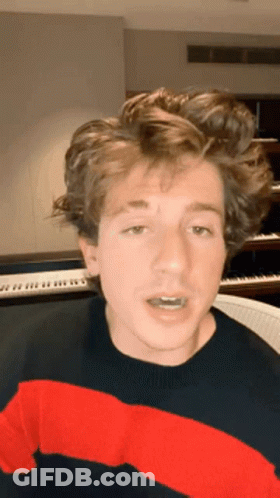 A Young Man Wearing A Red And Black Striped Sweater Is Sitting In Front Of A Piano Keyboard . GIF