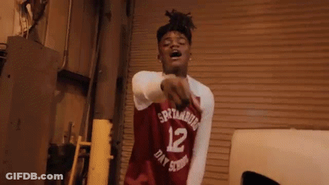 A Young Man Wearing A Red Basketball Jersey With The Number 12 On It Is Pointing At The Camera . GIF