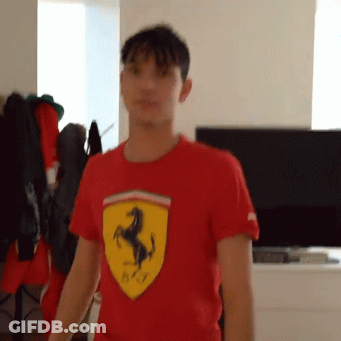 A Young Man Wearing A Red Ferrari Shirt Is Standing In Front Of A Television . GIF