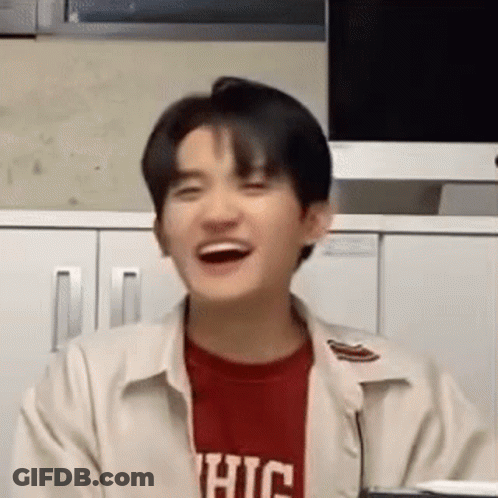 A Young Man Wearing A Red Shirt And A White Jacket Is Laughing In Front Of A Computer Monitor . GIF