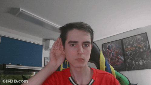A Young Man Wearing A Red Shirt Is Covering His Ear With His Hand GIF