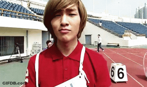 A Young Man Wearing A Red Shirt Is Standing On A Track With A Number 66 Block In Front Of Him GIF