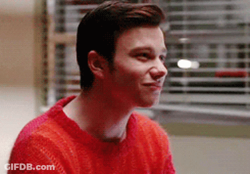 A Young Man Wearing A Red Sweater Is Smiling While Sitting In Front Of A Window . GIF