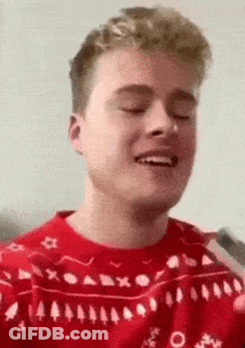 A Young Man Wearing A Red Sweater With Trees On It Is Smiling With His Eyes Closed . GIF