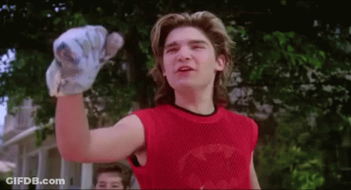 A Young Man Wearing A Red Tank Top Is Holding A Baseball Bat In His Hand . GIF