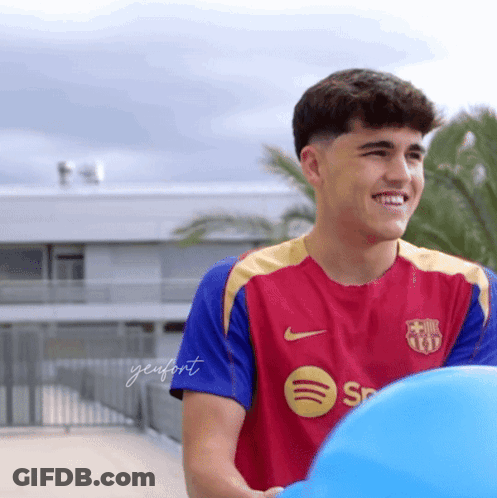 A Young Man Wearing A Spotify Shirt Smiles While Holding A Blue Ball GIF