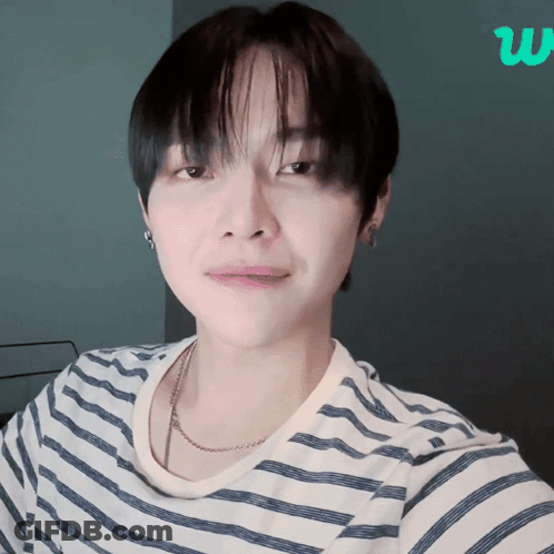 A Young Man Wearing A Striped Shirt And A Necklace Looks At The Camera GIF
