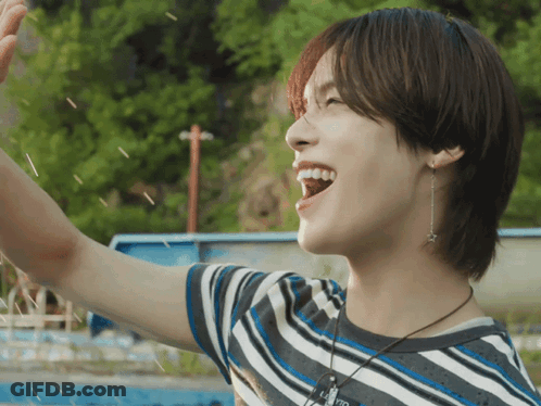 A Young Man Wearing A Striped Shirt And A Necklace With A Star On It Is Smiling GIF