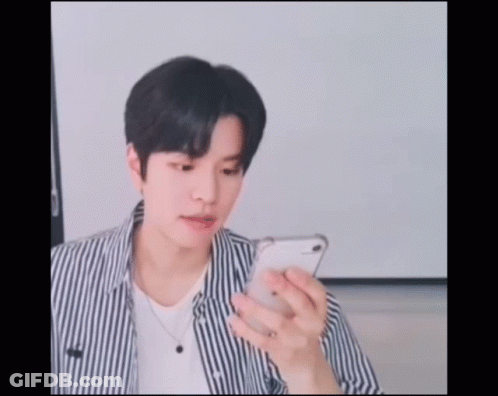 A Young Man Wearing A Striped Shirt Is Looking At His Phone GIF
