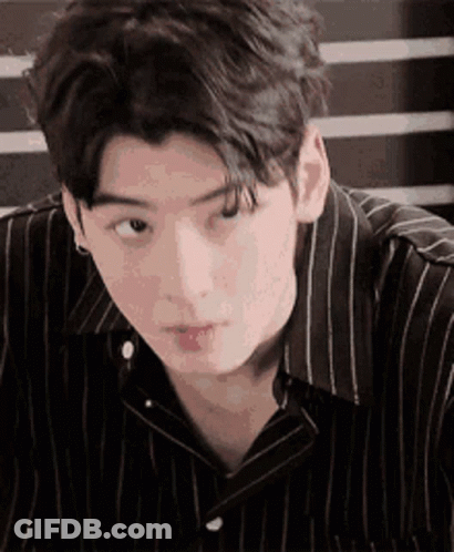 A Young Man Wearing A Striped Shirt Is Looking At The Camera . GIF