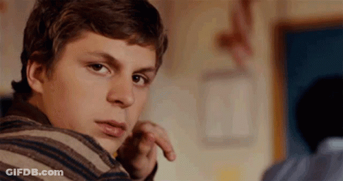 A Young Man Wearing A Striped Sweater Is Looking Over His Shoulder At The Camera . GIF
