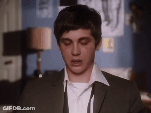 A Young Man Wearing A Suit And Tie Is Looking Down With His Eyes Closed GIF