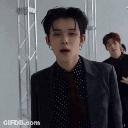 A Young Man Wearing A Suit And Tie Is Standing In A Room With Other Men . GIF