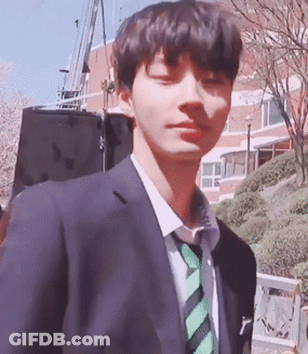 A Young Man Wearing A Suit And Tie Is Standing In Front Of A Building GIF