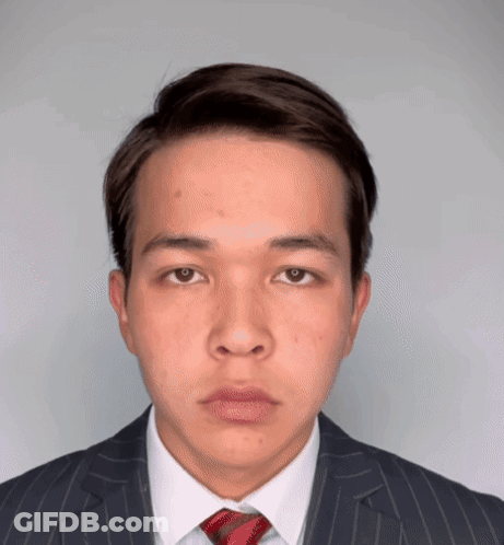 A Young Man Wearing A Suit And Tie Looks At The Camera GIF