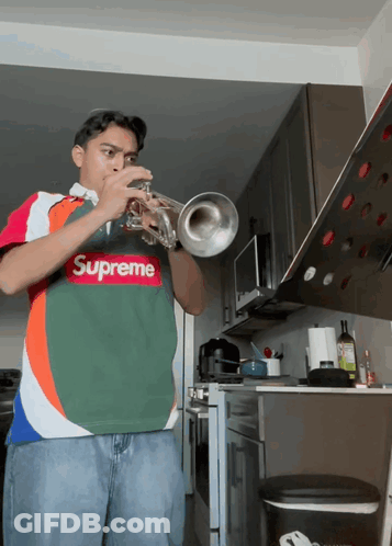 A Young Man Wearing A Supreme Shirt Plays A Trumpet GIF