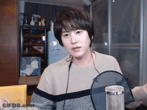 A Young Man Wearing A Sweater And Headphones Is Standing In Front Of A Microphone GIF