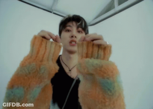 A Young Man Wearing A Sweater With A Necklace Around His Neck Looks At The Camera GIF