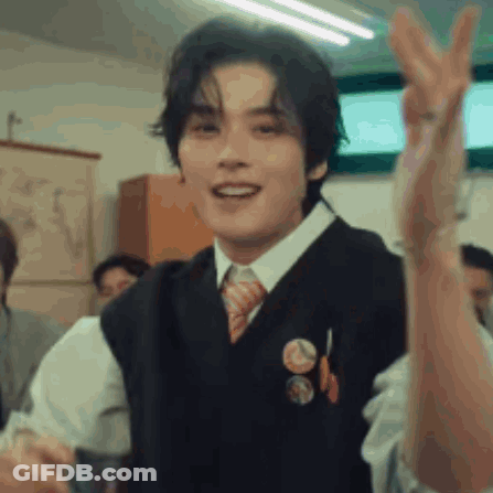 A Young Man Wearing A Vest And Tie Is Giving A Peace Sign In A Classroom . GIF
