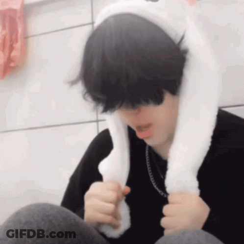 A Young Man Wearing A White Bunny Ear Hat Is Sitting Down . GIF