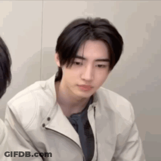A Young Man Wearing A White Jacket And A Blue Shirt Is Looking At The Camera . GIF