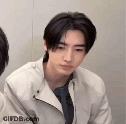 A Young Man Wearing A White Jacket Is Looking At The Camera . GIF