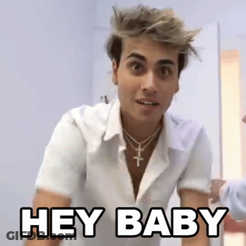 A Young Man Wearing A White Shirt And A Cross Necklace Is Standing In A Room And Saying `` Hey Baby '' . GIF