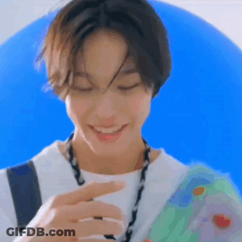A Young Man Wearing A White Shirt And A Necklace Is Smiling While Holding A Blue Balloon . GIF