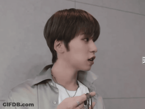 A Young Man Wearing A White Shirt And A Necklace Looks To The Side GIF