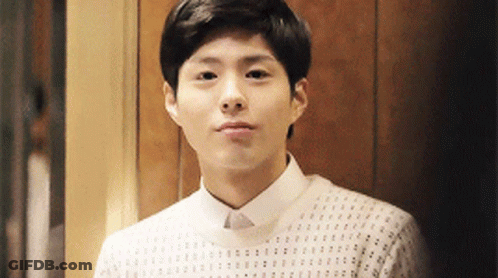 A Young Man Wearing A White Shirt And Sweater Is Looking At The Camera . GIF