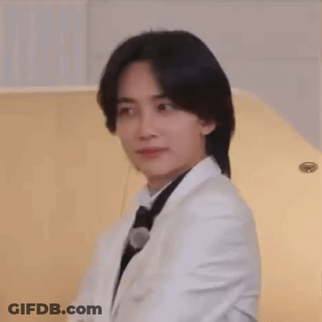 A Young Man Wearing A White Suit And Black Tie Is Sitting In Front Of A Piano . GIF