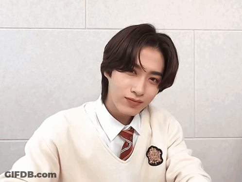 A Young Man Wearing A White Sweater And A Red Tie Winks At The Camera GIF