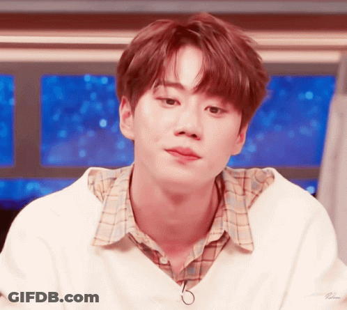 A Young Man Wearing A White Sweater And Plaid Shirt Looks To The Side GIF