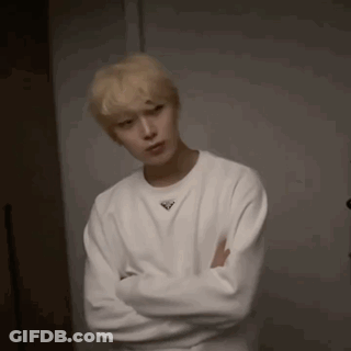 A Young Man Wearing A White Sweater With His Arms Crossed . GIF