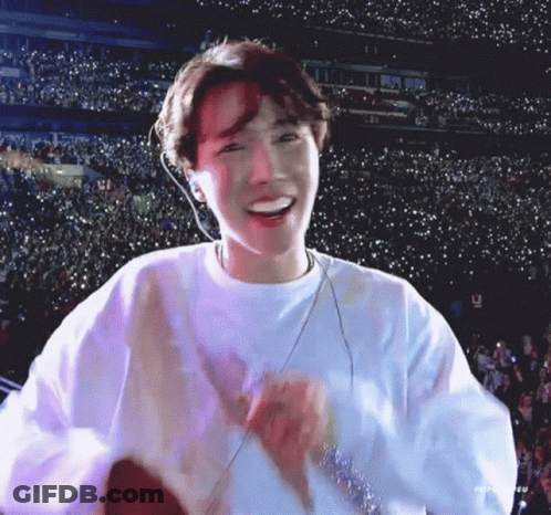 A Young Man Wearing A White Sweatshirt Is Smiling In Front Of A Crowd . GIF