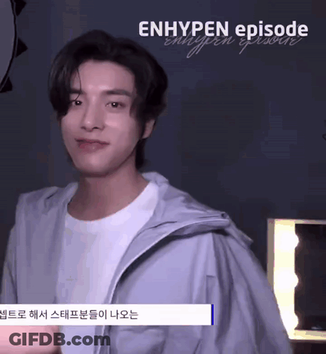 A Young Man Wearing A White T-Shirt And A Gray Jacket Is Standing In Front Of A Mirror And Smiling . GIF