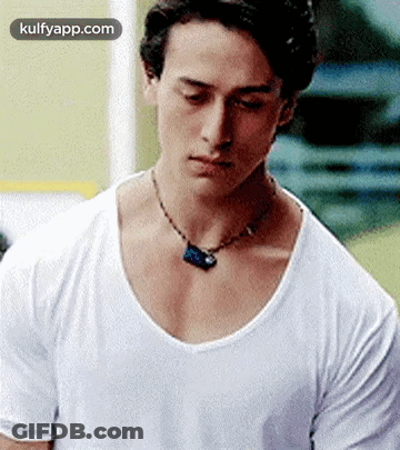 A Young Man Wearing A White T-Shirt And A Necklace Is Looking Down . GIF