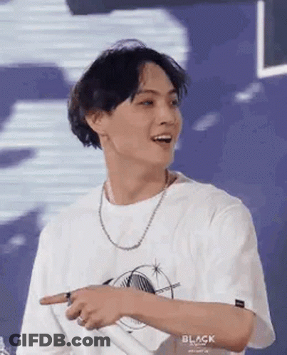 A Young Man Wearing A White T-Shirt And A Necklace Is Pointing At Something With His Finger . GIF