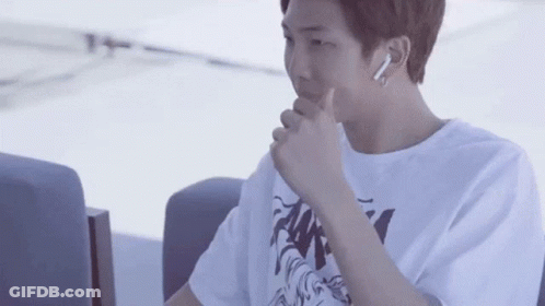 A Young Man Wearing A White T-Shirt And Ear Buds Is Sitting In A Chair . GIF