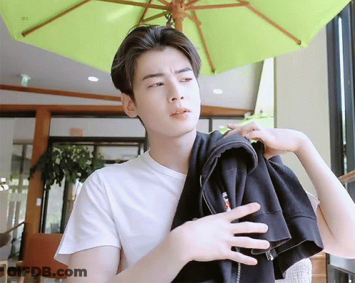 A Young Man Wearing A White T-Shirt Is Holding A Black Jacket Over His Shoulder . GIF