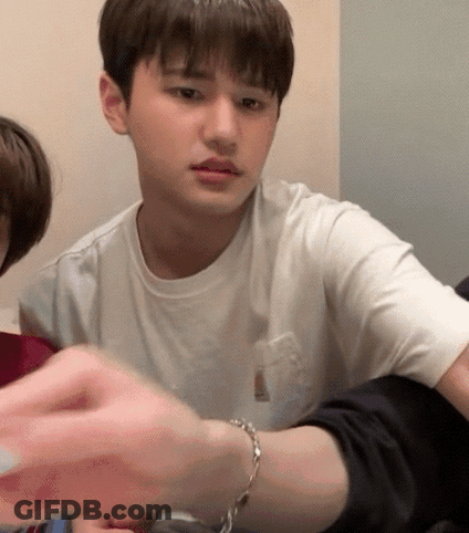 A Young Man Wearing A White T-Shirt Is Sitting At A Table With A Bracelet On His Wrist . GIF