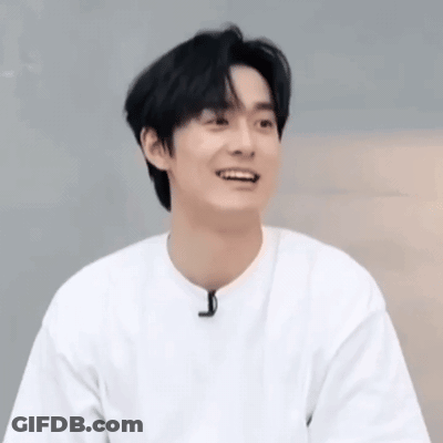 A Young Man Wearing A White T-Shirt Is Smiling And Looking At The Camera . GIF