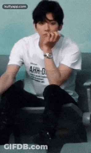 A Young Man Wearing A White T-Shirt That Says Ahh-D Is Sitting On A Chair GIF