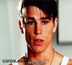 A Young Man Wearing A White Tank Top And A Necklace Says Yes Ma 'Am . GIF