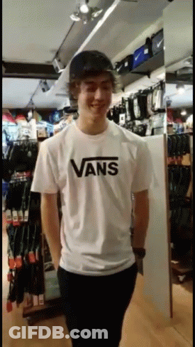 A Young Man Wearing A White Vans T-Shirt Stands In A Store GIF