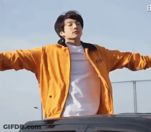 A Young Man Wearing A Yellow Jacket And A White Shirt Is Standing In Front Of A Car With His Arms Outstretched . GIF