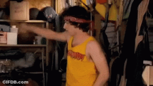 A Young Man Wearing A Yellow Tank Top And A Bandana Is Standing In A Closet . GIF