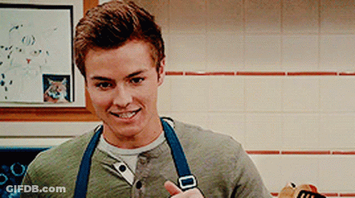 A Young Man Wearing An Apron Is Giving A Thumbs Up In A Kitchen GIF